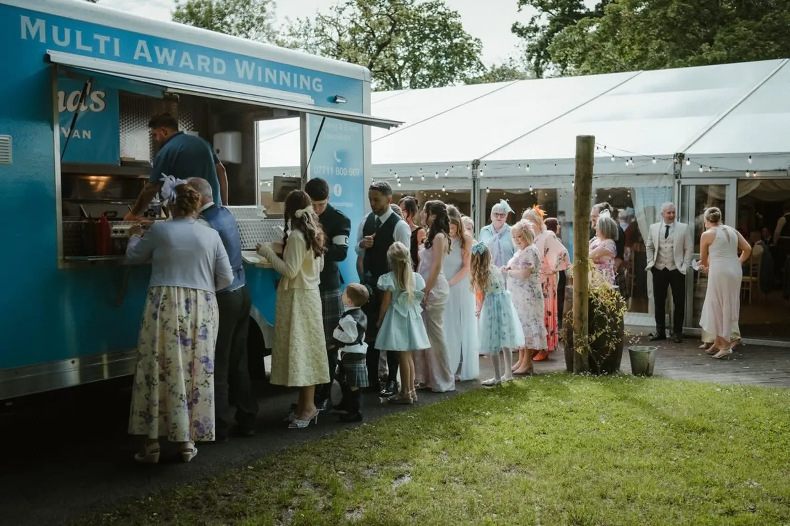 Wedding guests queuing at Joanna's Chippy Van beside a marquee reception